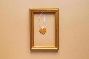 día de san valentín o concepto romántico de boda. marco de fotos dorado con corazón de madera en el interior sobre fondo beige.