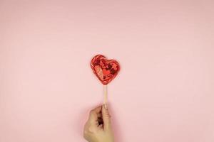 Female hands holding red sequin heart on pink background. Creative minimal layout with copy space photo