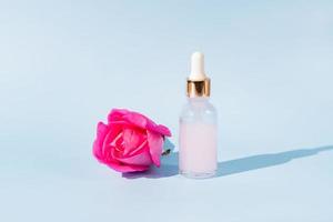 skincare natural rose essential oil product. Pink rose petals and cosmetic glass bottle with dropper for moisturizing serum anti aging product. photo