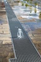 Vertical water streams of dry fountain, close up view. Streams flowing out of stainless grate photo