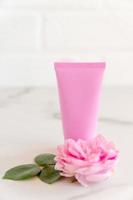 pink tube with rose face or body cream or scrub decorated with pink core flowers. Skin care concept. Unbranding mockup photo