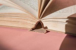 Open hardcover old book on pink background with copy space. Educational concept photo