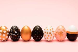 vista lateral de huevos de pascua decorados en rosa, blanco, negro y dorado en una fila sobre fondo rosa. telón de fondo de vacaciones de moda. foto