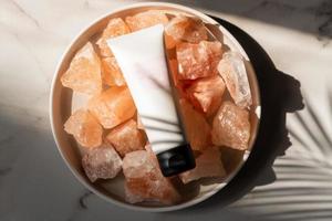 Unbranded tube with body care cosmetics lies on crystals of pink himalayan salt. Spa and wellnes concept photo