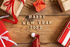 feliz año nuevo 2022. cita hecha de letras de madera y números 2022 sobre fondo de madera con cajas de regalo multicolores. concepto creativo para la tarjeta de felicitación de año nuevo foto