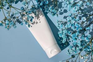 white cosmetic tube on a blue background withgypsophila flowers. The concept of a cream with natural ingrediant and not testing on animals. photo