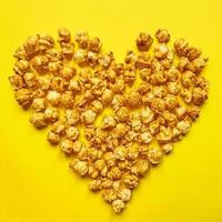 Caramel popcorn in heart shape on yellow background. Love popcorn concept. Sweet food photo