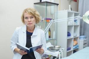 middle aged woman in white coat holding blue daily planner. Doctor female, medical professional photo