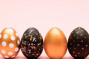 Side view of pink, white, black and golden decorated easter eggs in a row on pink background. Trendy holiday backdrop. photo