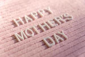 palabras feliz día de la madre en el tablero de letras de fieltro rosa. composición festiva con enfoque selectivo. foto