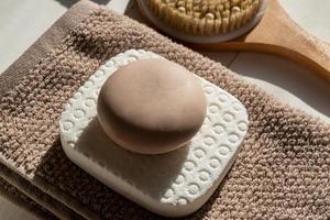 Close up of soap bar lies on towel background next to bamboo brush for massaging. Eco friendly space and personal hygiene concept. photo