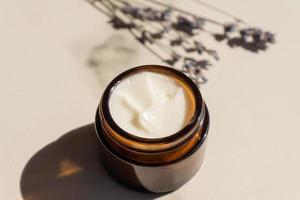 dark glass jar with cream of lavandula, flowers of dried purple lavender blossom on marble table. Herbal aromatherapy and skincare. photo