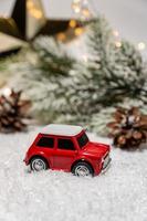 Miniature red toy car with spruce trees. Winter Holidays background. Christmas concept, holiday delivery. Christmas decorations and bokeh lights. photo