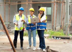 Female construction engineer holds computer laptop meeting with architect teamwork. Multiracial people group wear safety hardhat using laptop brainstorming on housing development at construction site photo