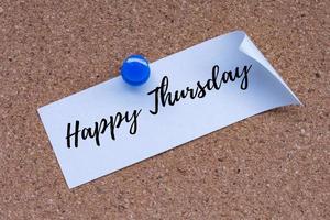 Happy Thursday text on white stick note and pinned to a cork notice board. photo