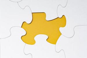 White jigsaw puzzle with some missing pieces on yellow background. photo