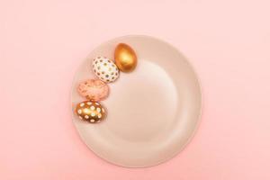 Top view of pink, white and golden decorated eeaster eggs on pink plate on pink background. Trendy holiday backdrop photo