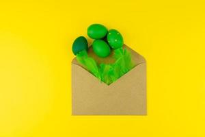 diseño de pascua de primavera con plumas verdes y huevos, sobre artesanal sobre fondo amarillo. copiar espacio para texto para texto. foto