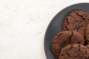 Top view, chocolate chip cookies on a black plate. white concrete background. From above. copy space photo