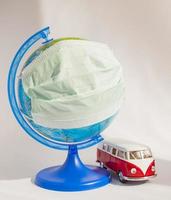 Coronavirus outbreak. World pandemia. Globe in medicine mask and travel bus on white background. Concept of traveling while covid-19. photo