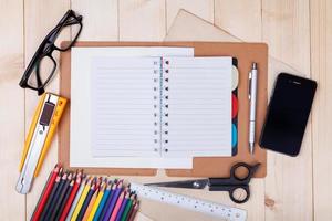 lugar de trabajo con lápices de colores y suministros, cuaderno, anteojos en mesa de madera foto