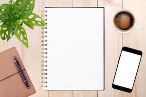 un cuaderno en blanco abierto, un teléfono inteligente con bolígrafo y una taza de café en la mesa de madera. foto