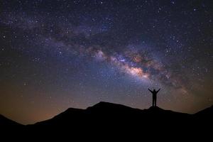 landscape with milky way, Night sky with stars and silhouette of a standing sporty man with raised up arms on high mountain. photo