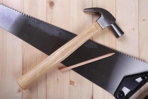 handsaw, claw hammer and pencil on wooden desk background photo