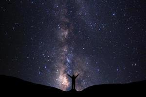 Milky way galaxy with stars and silhouette of a standing happy man, Long exposure photograph, with grain. photo