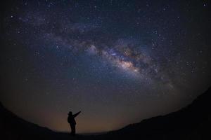 A Man is standing next to the milky way galaxy pointing on a bright star, Long exposure photograph, with grain. photo