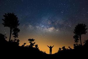 galaxia vía láctea y silueta de un hombre feliz de pie en el bosque, fotografía de larga exposición, con grano. foto