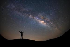 Panorama landscape with milky way, Night sky with stars and silhouette of a standing sporty man with raised up arms on high mountain. photo