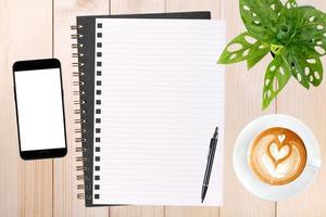 un cuaderno en blanco abierto, un teléfono inteligente con bolígrafo y una taza de café con leche en una mesa de madera. foto
