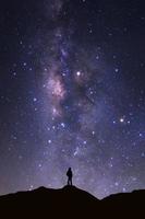 paisaje con vía láctea, cielo nocturno con estrellas y silueta de hombre parado en alta montaña foto