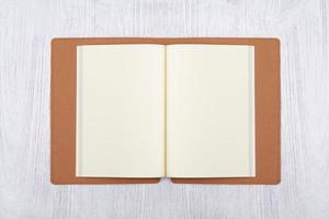 Open brown notebook on white wooden table, top view photo