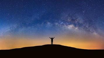 Panorama landscape with milky way, Night sky with stars and silhouette of a standing sporty man with raised up arms on high mountain. photo