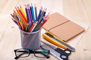 Workplace with colored pencils and supplies, notebook, eyeglass on wooden table photo