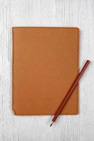 brown notebook and a pencil on white wooden table, top view photo