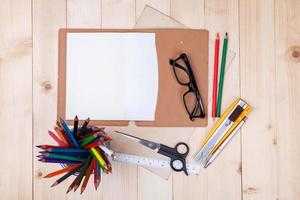 lugar de trabajo con lápices de colores y suministros, cuaderno, anteojos en mesa de madera foto