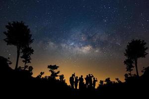 paisaje con vía láctea, cielo nocturno con estrellas y silueta de gente feliz parada en el bosque, fotografía de larga exposición, con grano. foto