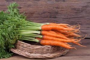Bunch of fresh carrots with green leaves over wooden background photo