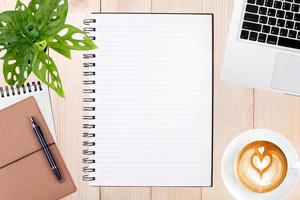 An open blank notebook, laptop with pen and a cup of coffee on wooden table. photo