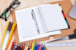 Workplace with colored pencils and supplies, laptop, notebook, eyeglass on wooden table photo