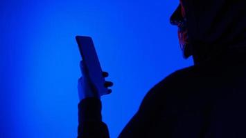 Anonymous hacker and face mask with smartphone in hand. photo