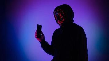 Anonymous hacker and face mask with smartphone in hand. photo