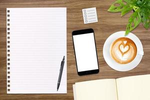 un cuaderno en blanco abierto, un teléfono inteligente con bolígrafo y una taza de café con leche en una mesa de madera. foto