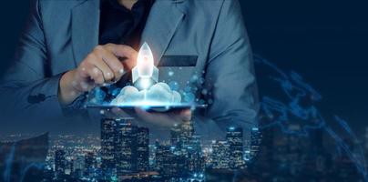 Startup business concept. Businessman holding a tablet, rocket launching and soar flying out from screen, starting a business, growing business, modern technology, hologram, network connection. photo