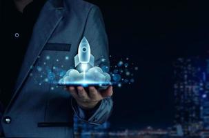 Startup business concept. Businessman holding a tablet, rocket launching and soar flying out from screen, starting a business, growing business, modern technology, hologram, network connection. photo