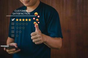 concepto de evaluación de la satisfacción del cliente, hombre que usa un teléfono inteligente sonriendo y con el pulgar hacia arriba, califica cinco estrellas, envía emoji y corazones sonrientes, cara sonriente satisfecha, excelente servicio, el cliente está feliz. foto