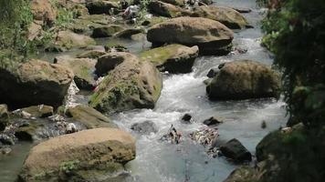 The river flows between the big rocks that beautify the river even though there is some garbage video